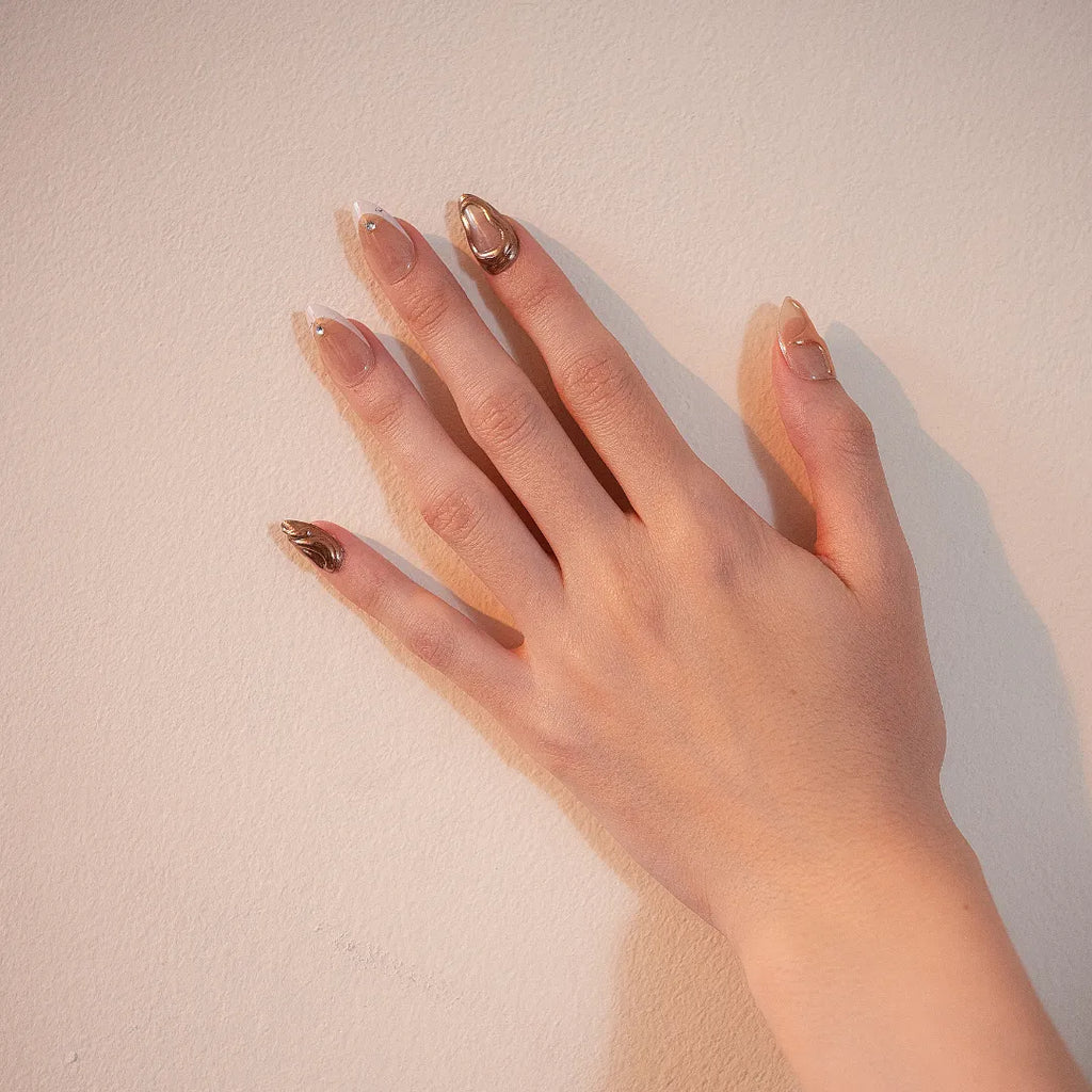 Premium nude chrome abstract press-on nails with metallic gold swirl accents, rhinestone details, and glossy almond shape