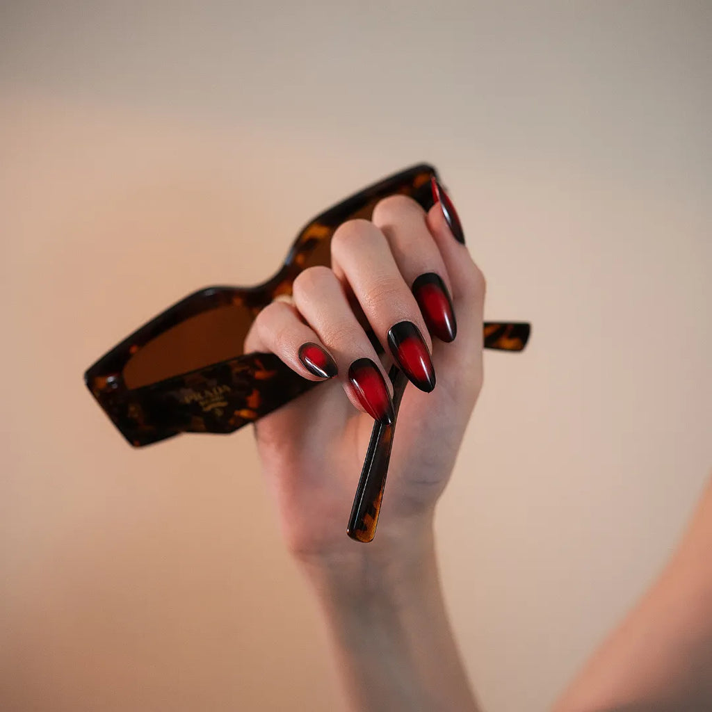 Long almond-shaped black and deep red ombré press-on nails with a glossy gradient finish by Soul Struck
