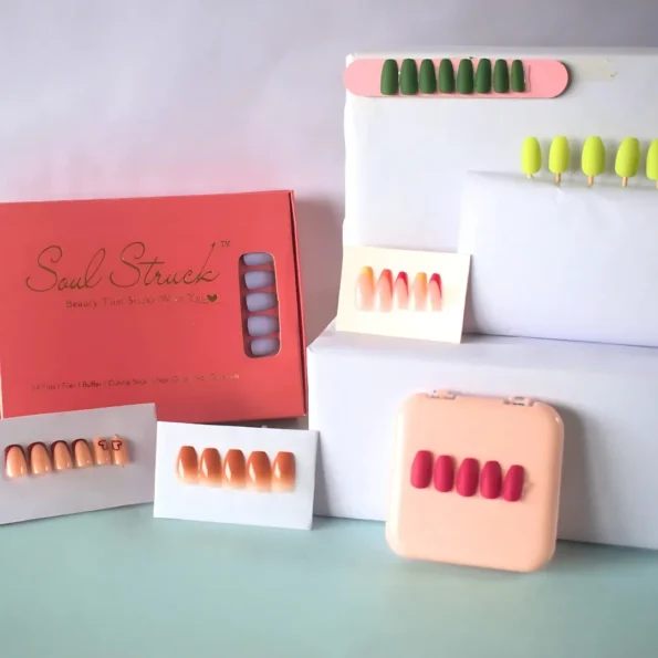 Hands with glossy pink and gold nails resting beside a watch, perfume, and silk scarf.